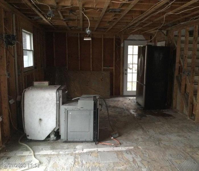 Kitchen tile, drywall, and fixtures have been removed, leaving wall and ceiling framing as well as the dishwasher, stove, and